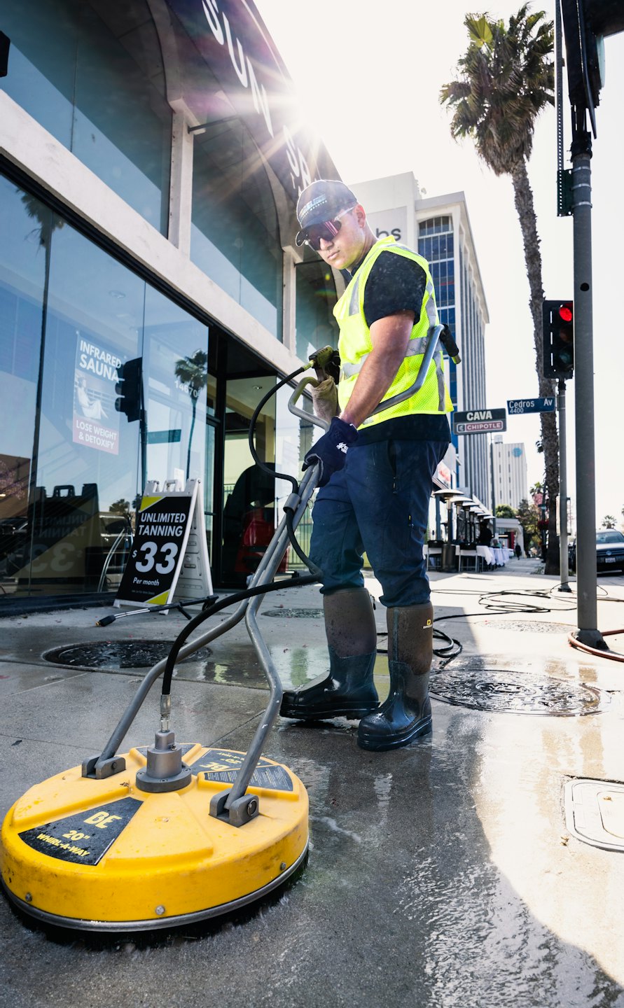 Man in yellow vest pressure washing a concrete sidewalk.