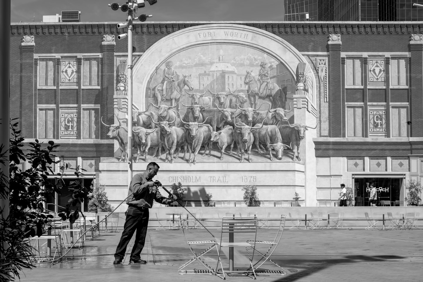 Worker power washes a patio near a building with a mural.