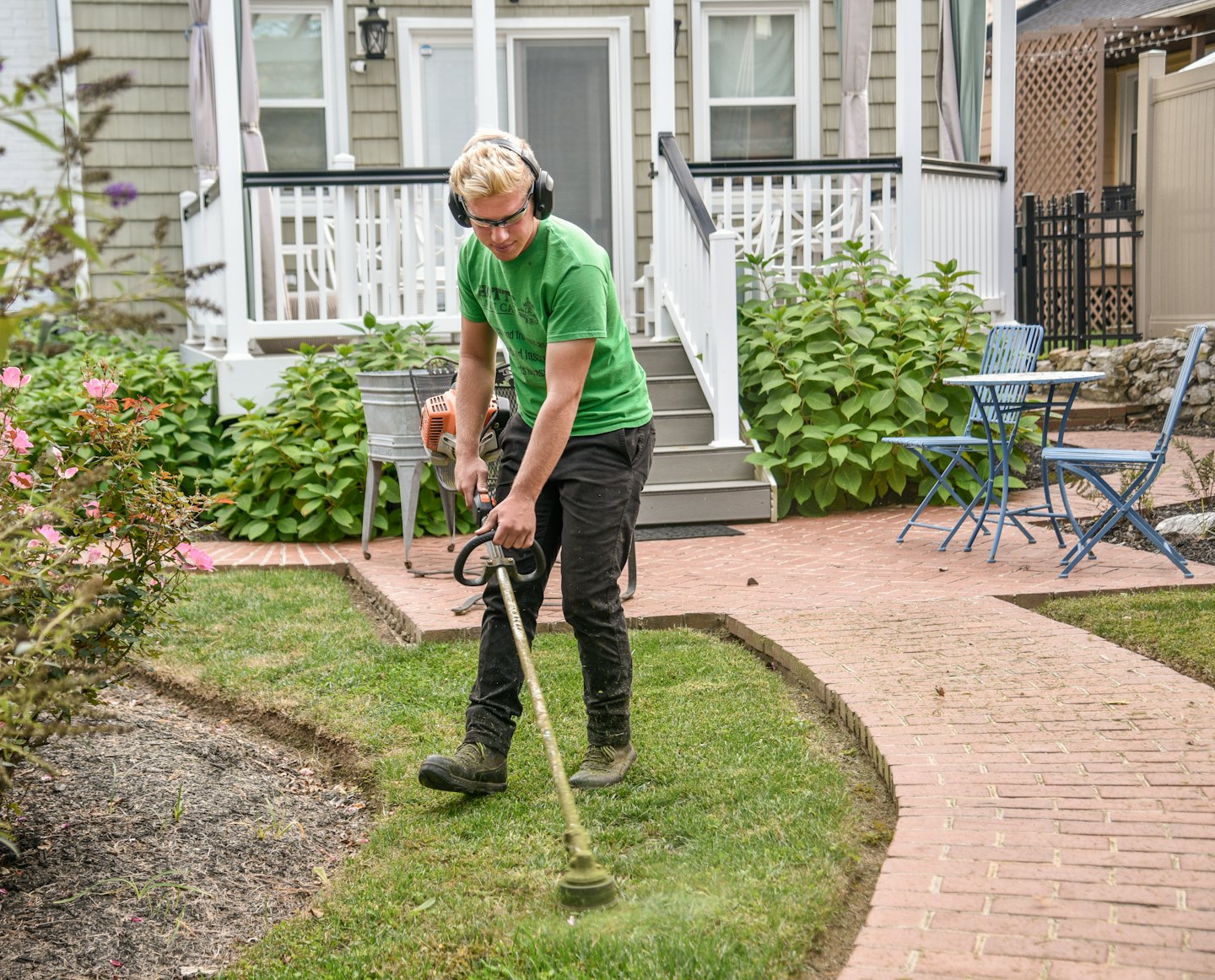 Man in green shirt trims lawn with string trimmer.