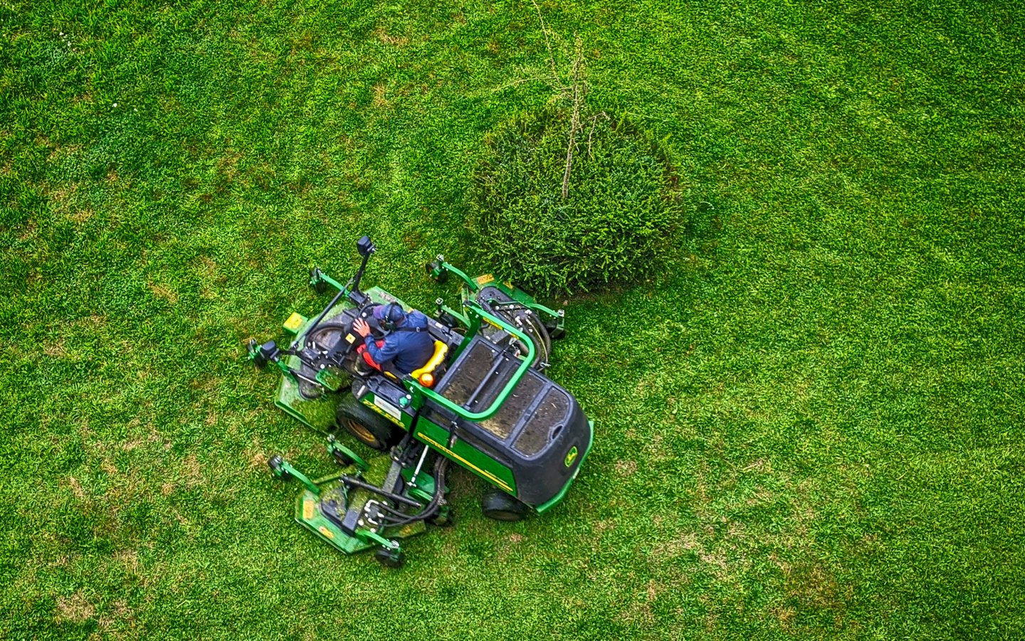 Professional mowing a large green lawn with a ride-on mower.